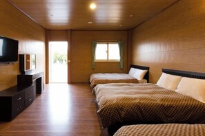 Habitación de hotel con paredes y suelos de madera, un televisor de pantalla plana sobre un aparador, dos camas con ropa de cama estampada y una ventana con cortinas.
