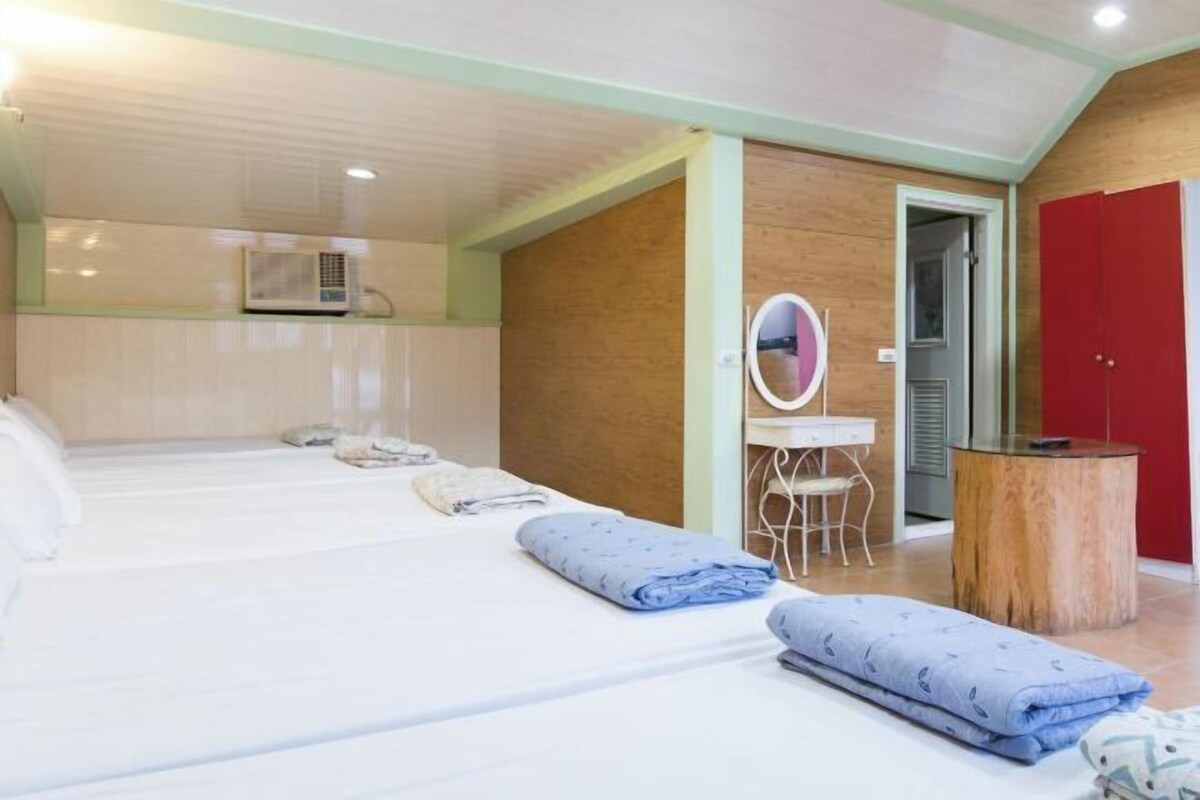 Una habitación de hotel con varias camas, una mesita pequeña, un espejo y un armario rojo.