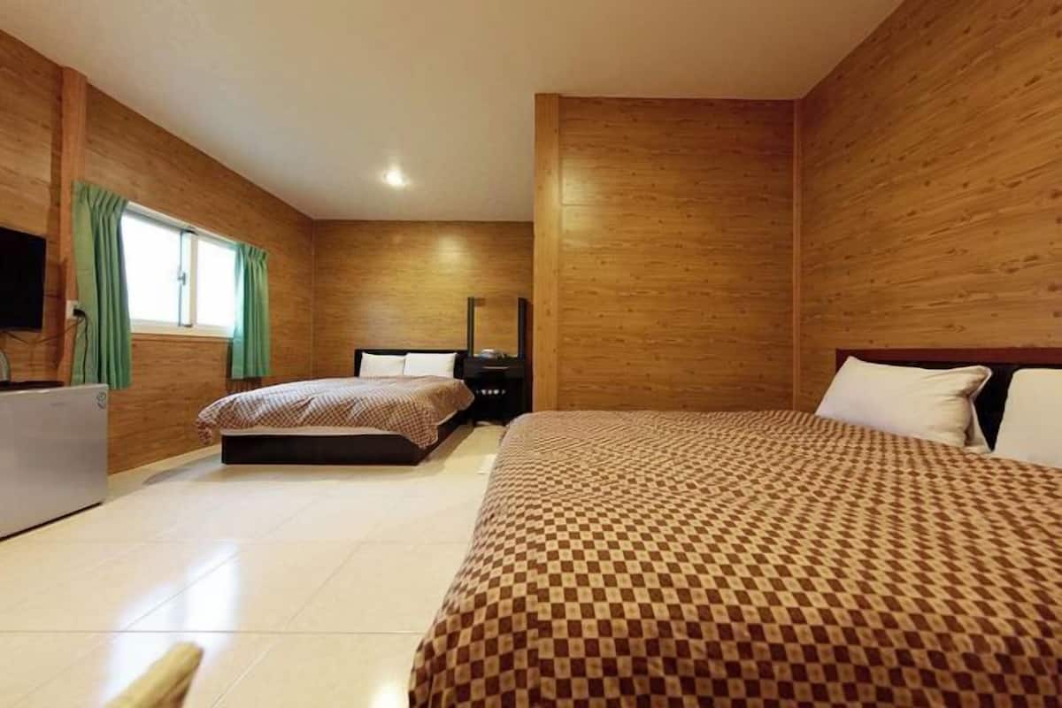 A room with wooden walls, two beds, a desk, and a television.