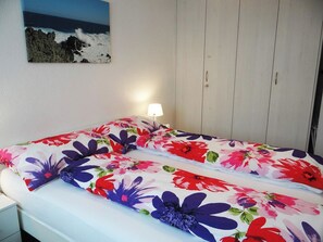 A bed with floral bedding, a bedside lamp, and a view of the sea through a window. - Sunnmatt West Wohnung 743 Appartement/Fewo 4-Bettwohnung by Interhome (Engelberg)