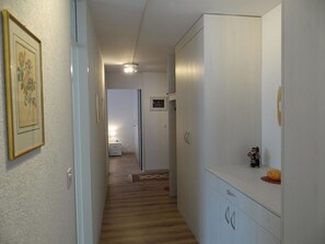 Un pasillo con suelo de madera, un armario blanco y un cuadro en la pared.