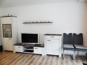 A living room with a TV, a cabinet with glass doors, a shelf with cups, and a chair. - Sunnmatt West Wohnung 743 Appartement/Fewo 4-Bettwohnung by Interhome (Engelberg)
