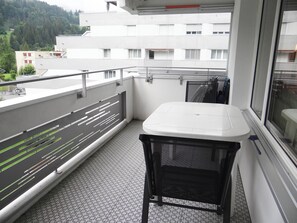 A balcony with a white table and a chair, a patterned floor, and a view of buildings and trees.
