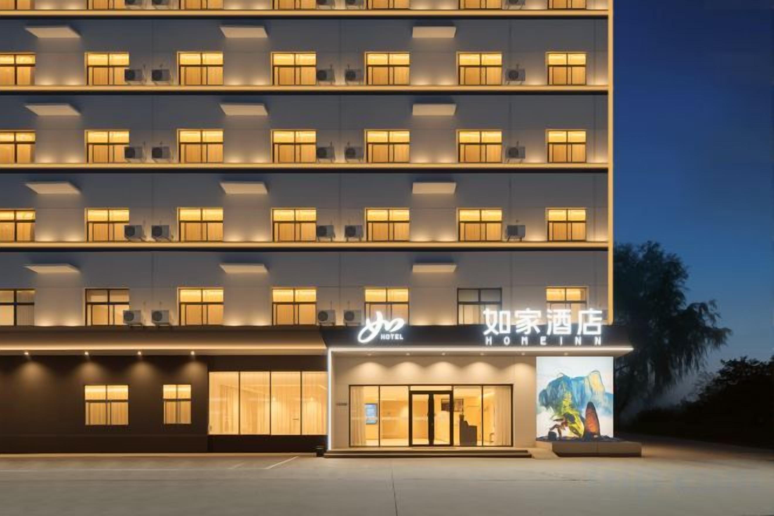 A multi-story hotel with a modern facade, illuminated windows, and a prominent entrance with a sign.