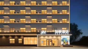 A multi-story hotel with a modern facade, illuminated windows, and a prominent entrance with a sign.
