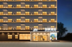 Un hotel de varios pisos con fachada moderna, ventanas iluminadas y una entrada destacada con un cartel.