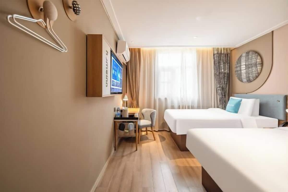 Une chambre d’hôtel avec deux lits, un bureau avec une lampe, une télévision et une fenêtre avec des rideaux.