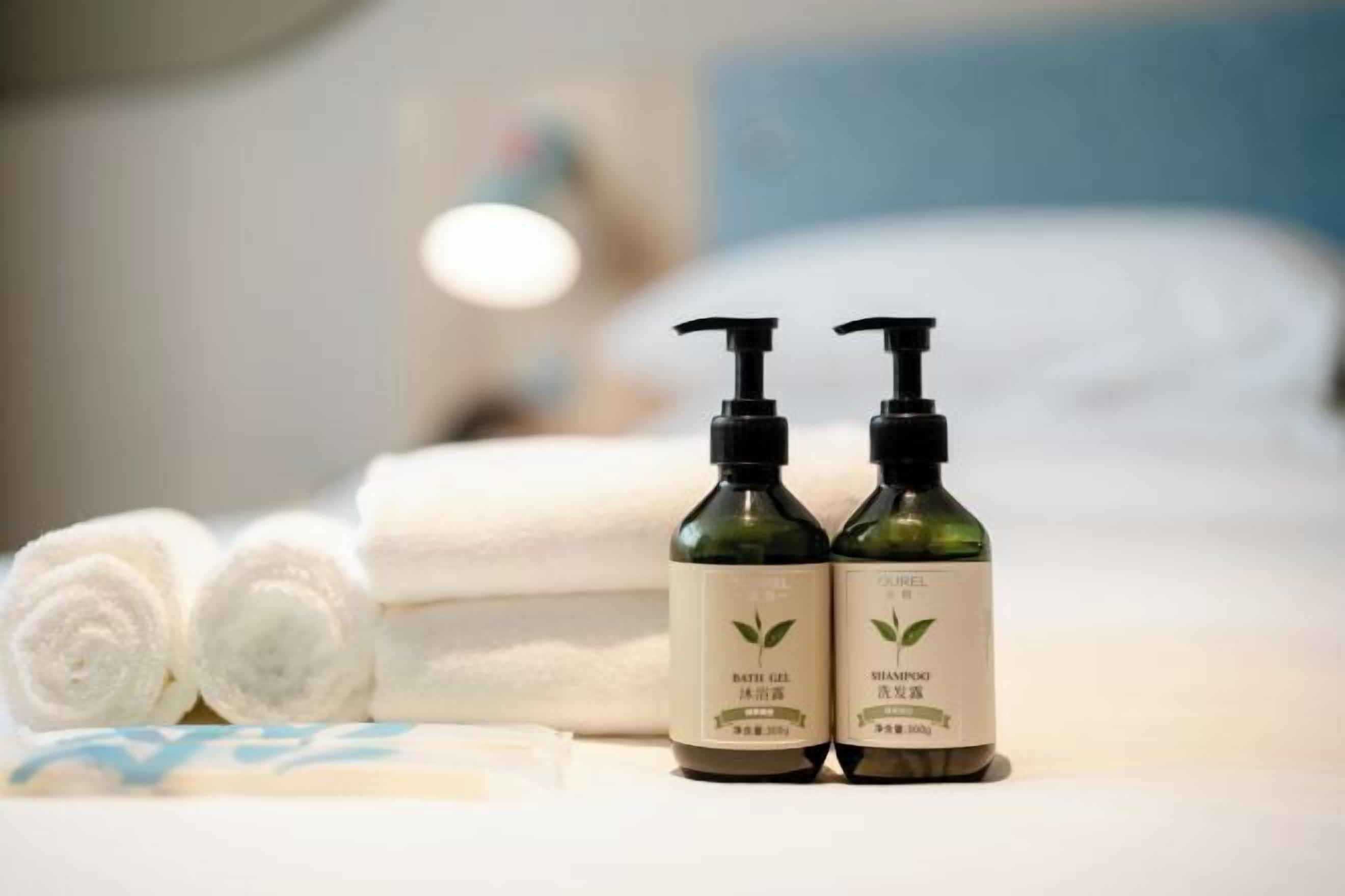 Dos botellas de gel de baño y champú sobre una cama con toallas enrolladas.