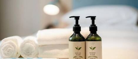 Dos botellas de gel de baño y champú sobre una cama con toallas enrolladas.