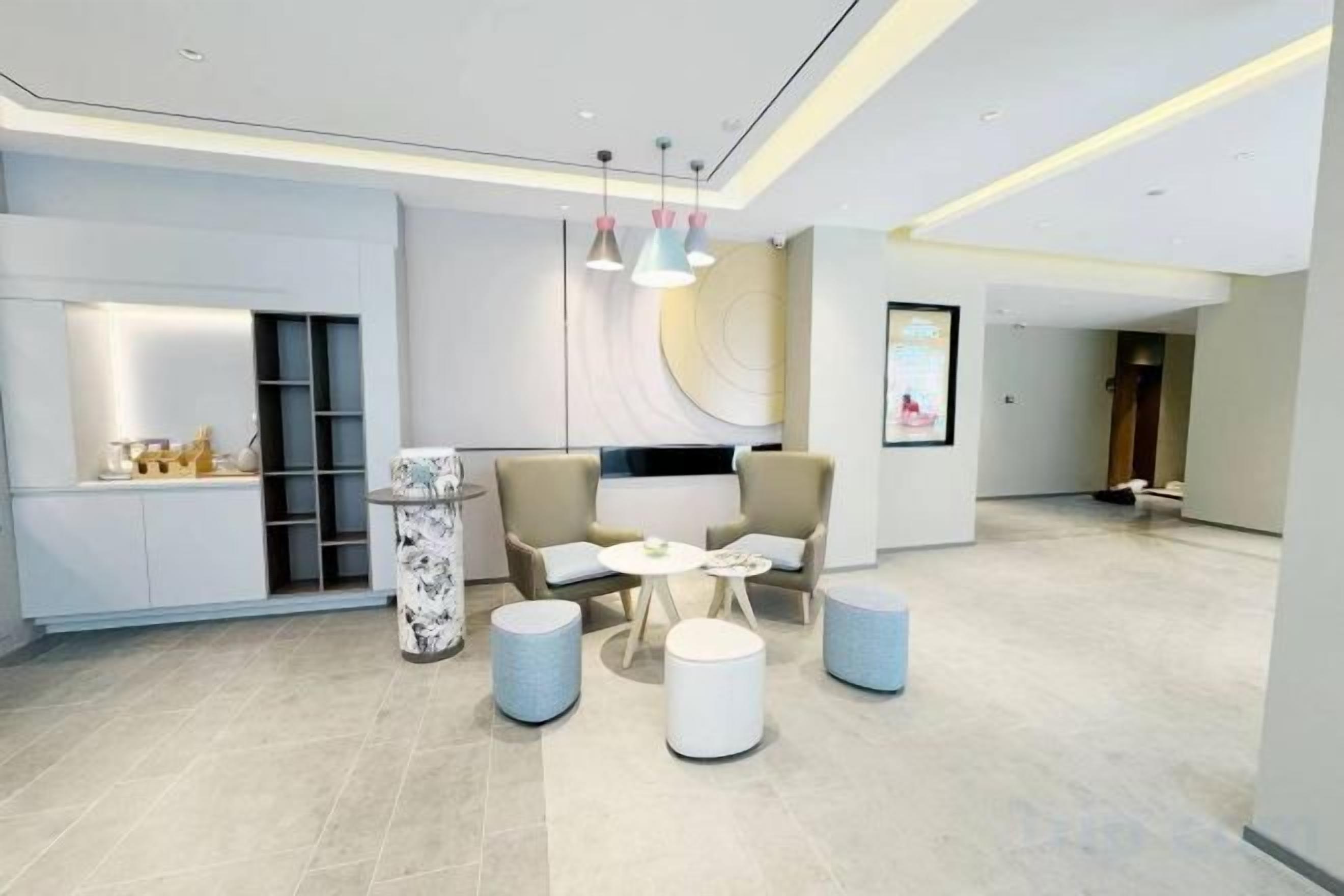 A modern hotel lobby with a seating area, a reception desk, and a large artwork on the wall.