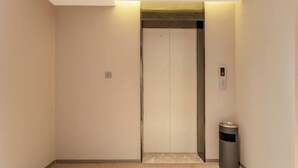 A narrow hallway with a closed elevator door and a trash bin to the right. - Home Inn (Huayin Huashan Scenic Area Branch) (Huayin)