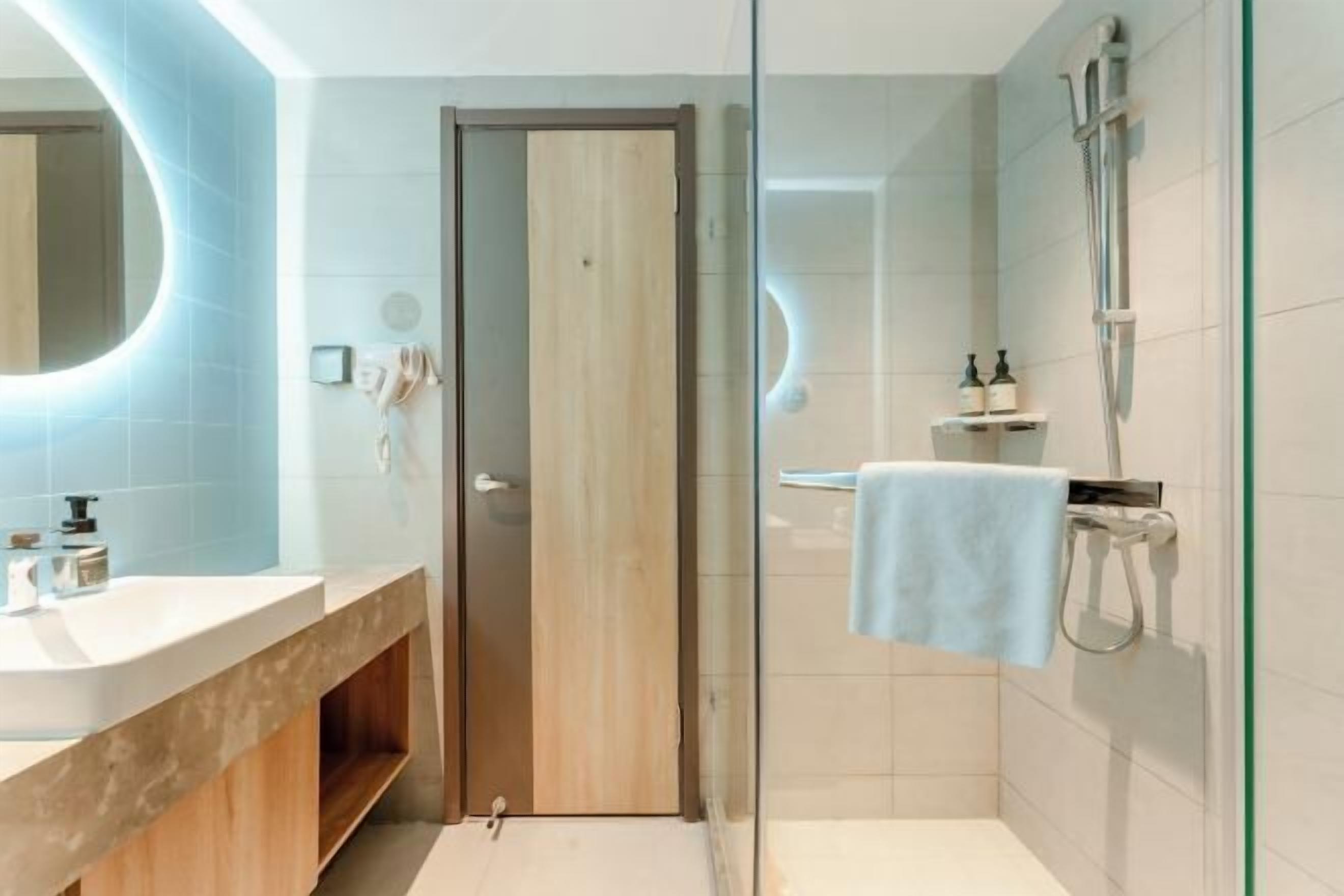 Une salle de bain moderne avec une douche à parois de verre, une porte en bois et un lavabo blanc doté d’un plan de travail en marbre.