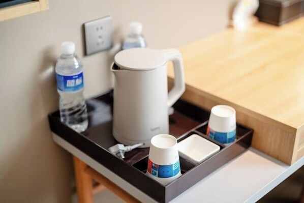 Mesita de noche en una habitación de hotel con una botella de agua, una taza blanca y una cafetera.