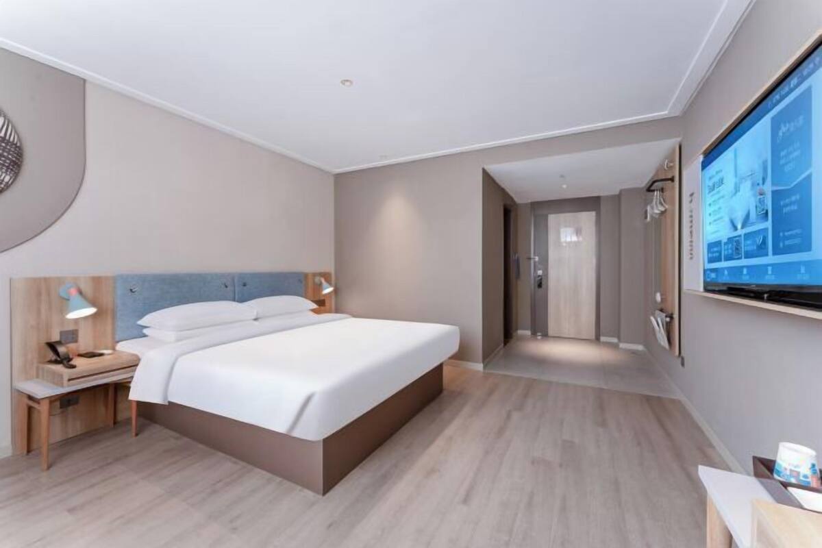 Une chambre d’hôtel moderne dotée d’un grand lit, d’un bureau, d’un téléviseur fixé au mur et d’un plancher en bois.