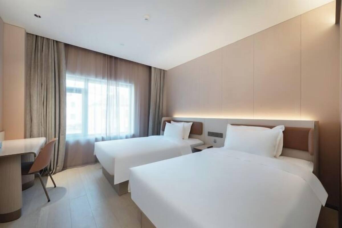 A hotel room with two beds, a desk, and a chair.
