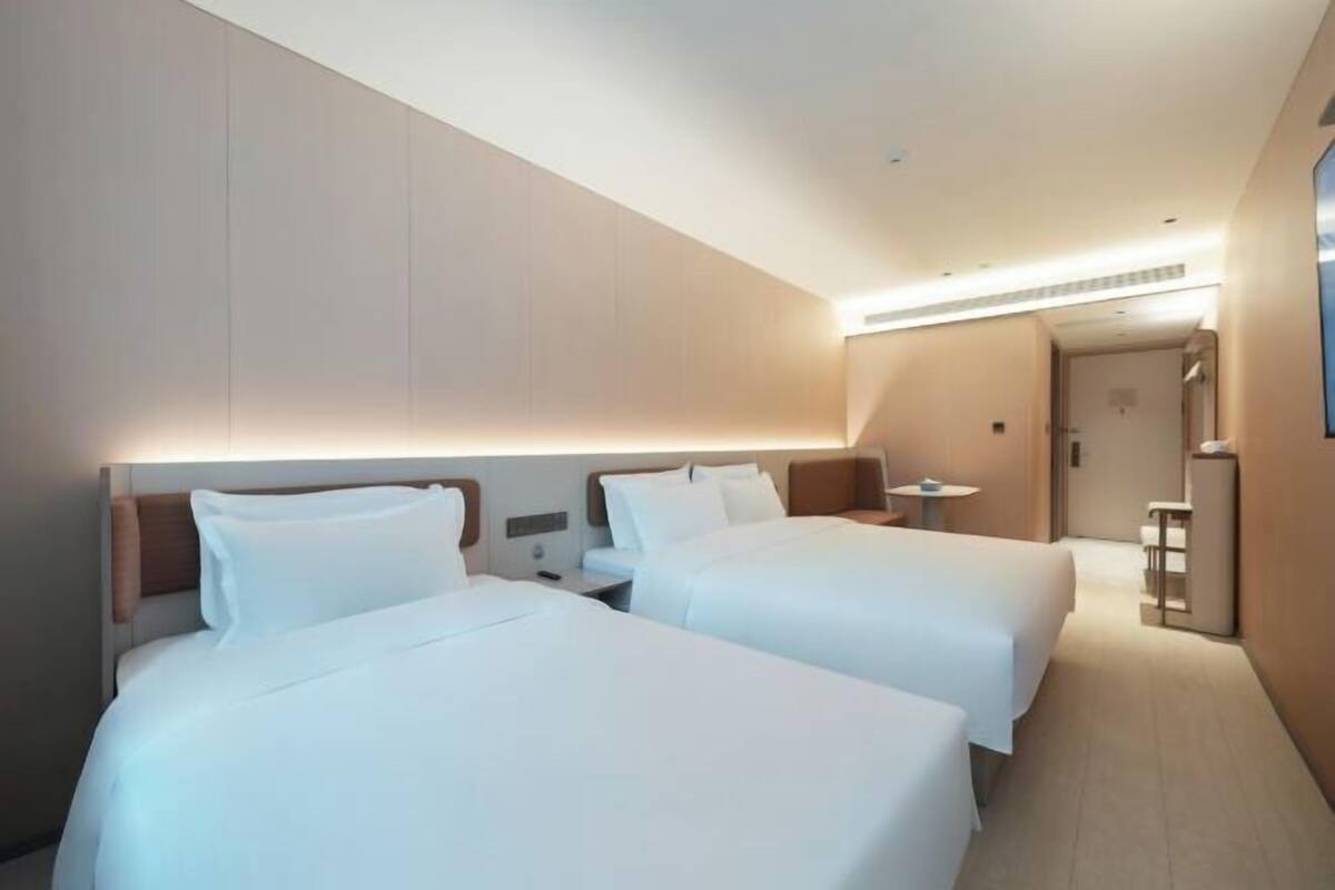 A hotel room with two beds, a small table, and a chair.
