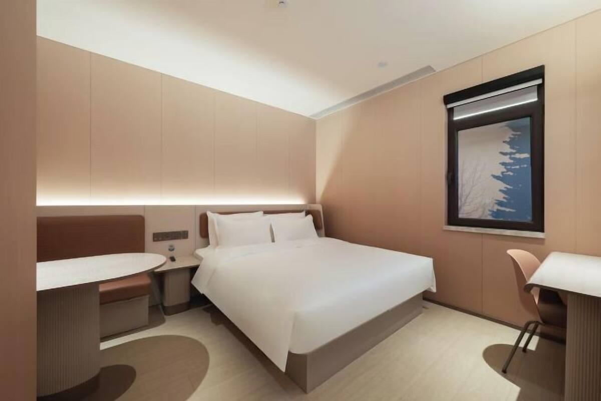 A modern hotel room with a bed, bedside tables, a desk, and a window with a view.