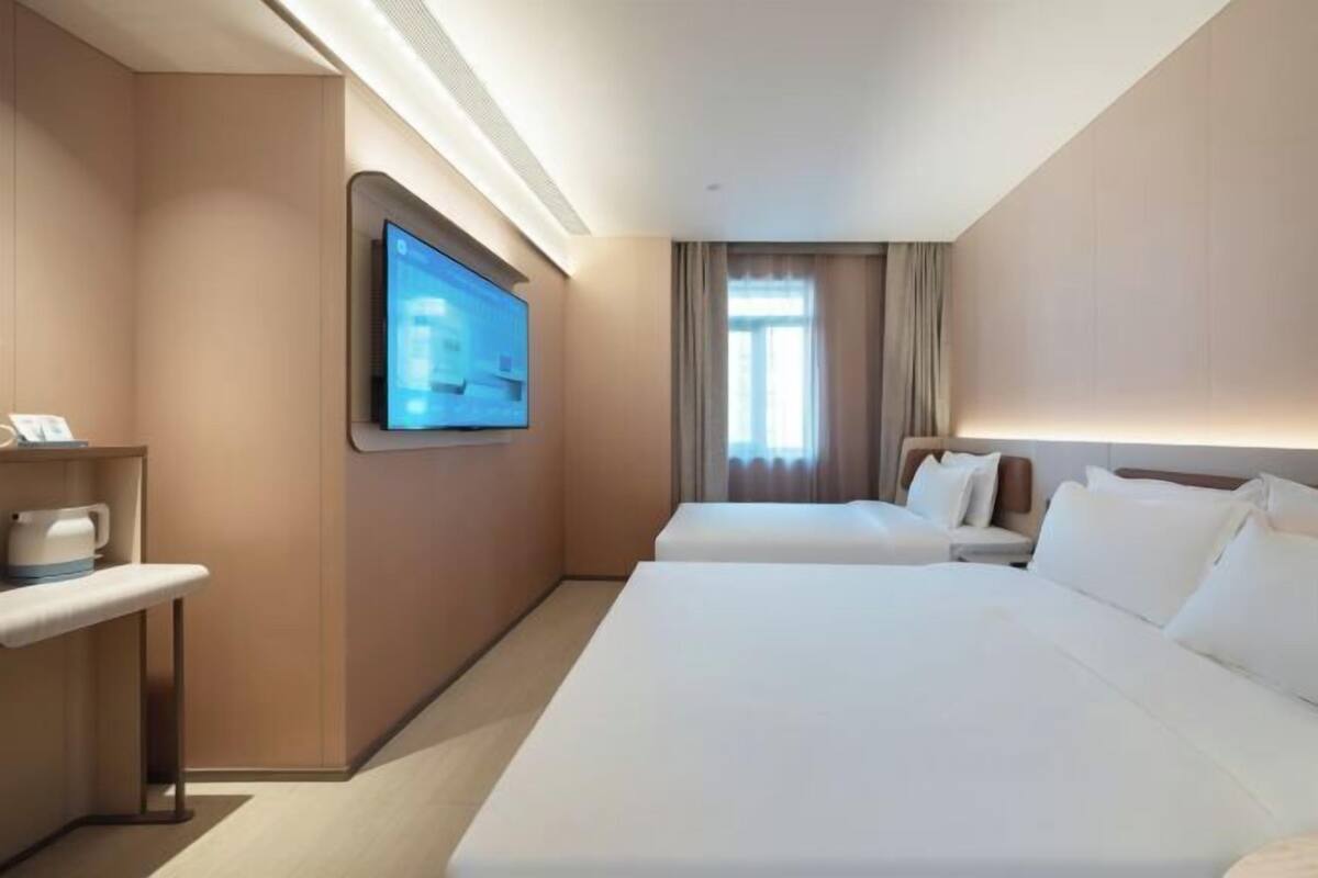 A hotel room with two beds, a TV, a bedside table, and a window with curtains.
