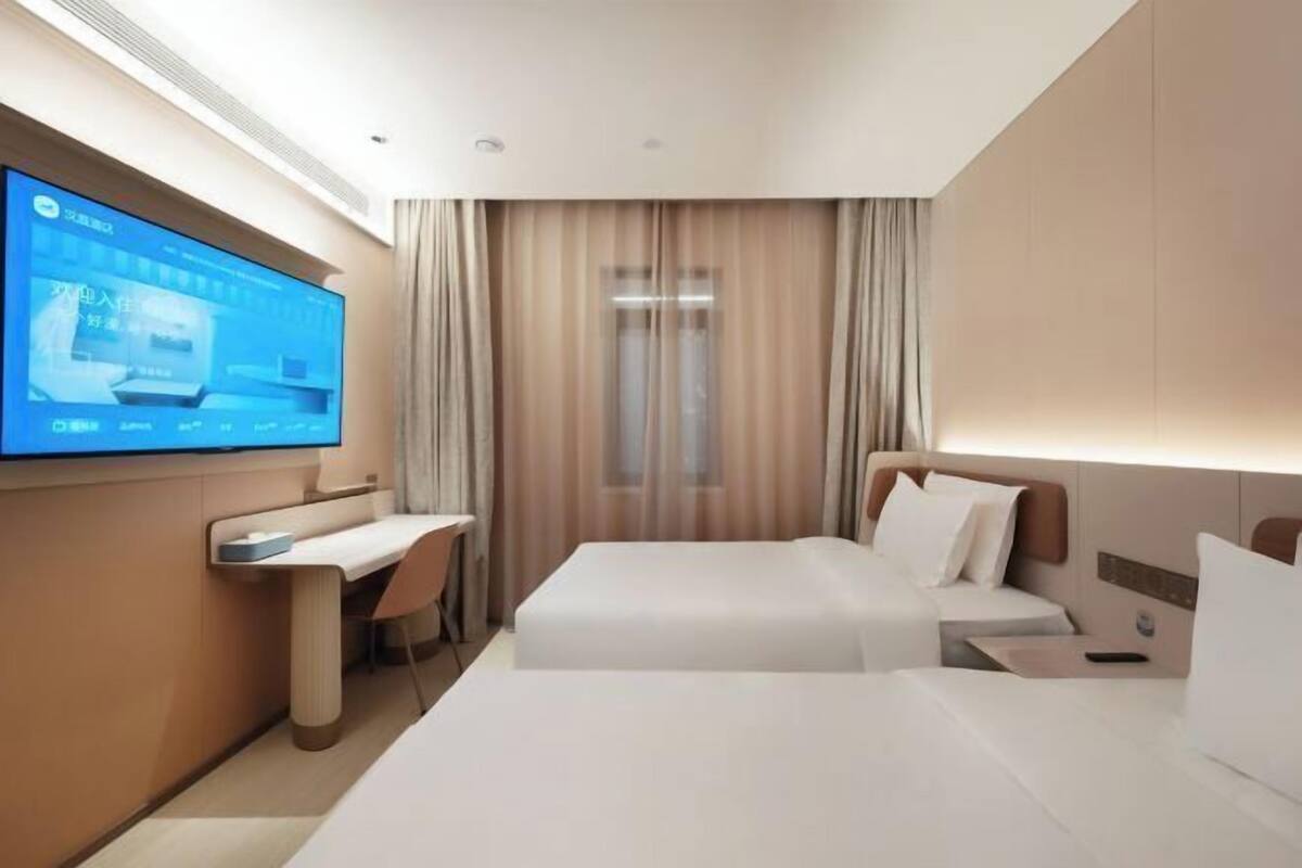 A hotel room with a bed, bedside tables, a desk, a chair, a TV mounted on the wall, and a window with curtains.