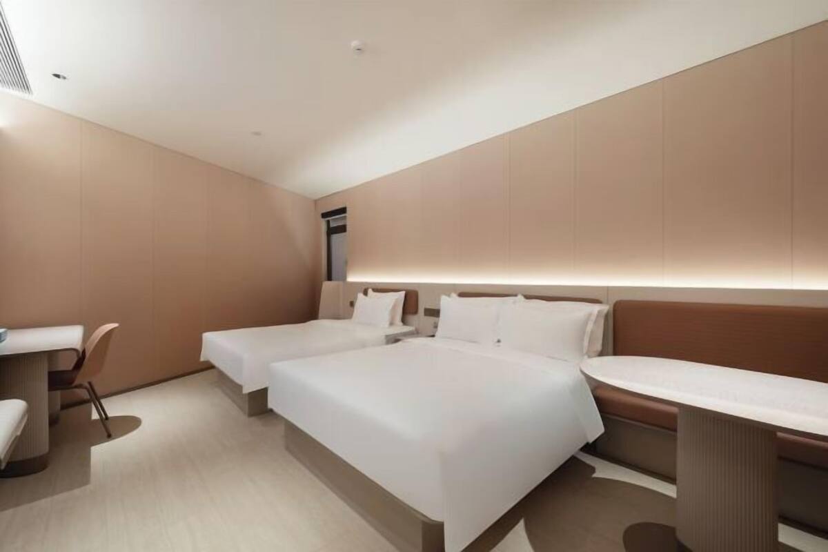 A modern hotel room with two beds, a desk, and a seating area.