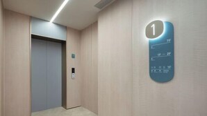 A hallway with a blue elevator sign, a door, and a wall-mounted control panel.