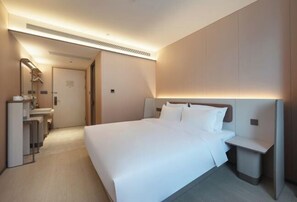 A hotel room with a large bed, bedside tables, a mirror, and a bathroom with a sink and toilet. - HanTing Hotel (Qingdao Zhanqiao Railway Station East Square) (Qingdao)