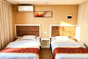 A hotel room with two beds, a nightstand, an air conditioning unit, and a small wall-mounted control panel.