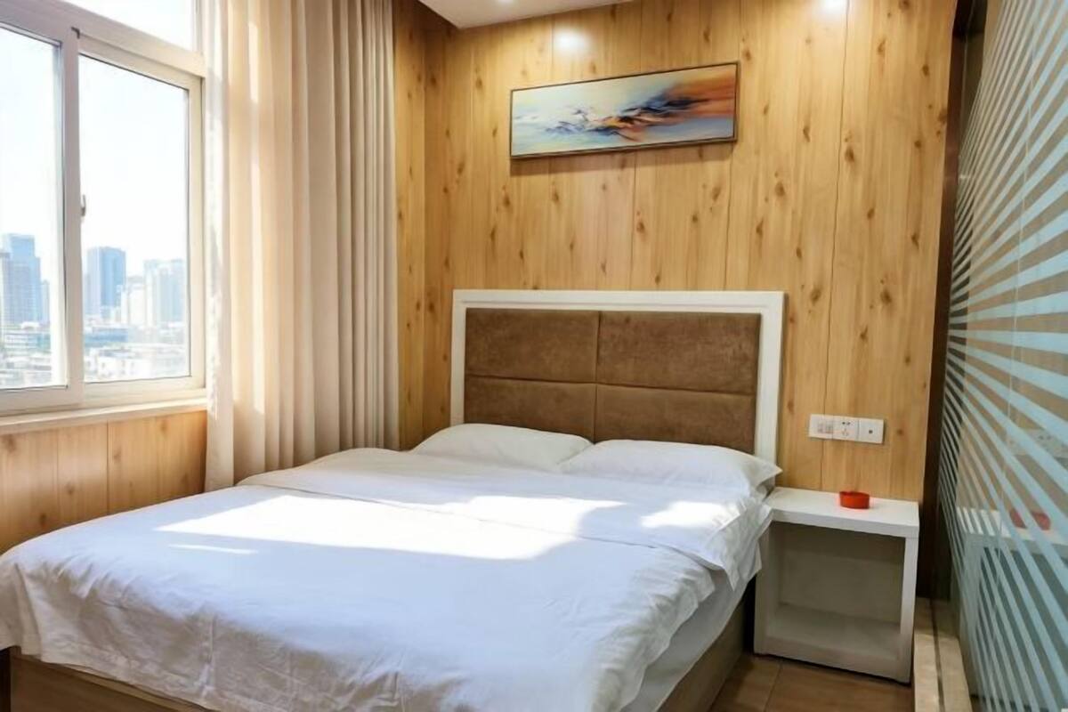 Una habitación de hotel con una cama, una mesita de noche, un cuadro en la pared y una ventana con cortinas.