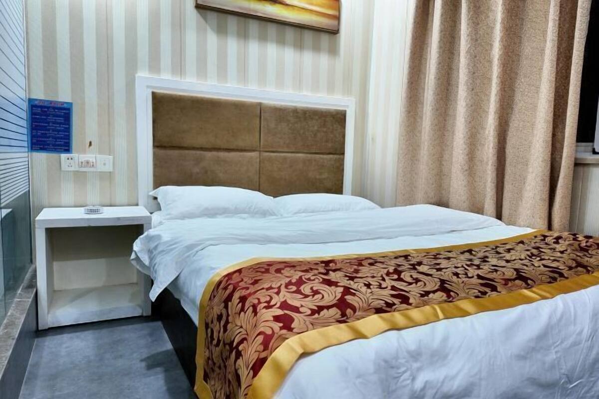 Habitación de hotel con cama, mesita de noche, un reloj en la pared y ventana con cortinas.