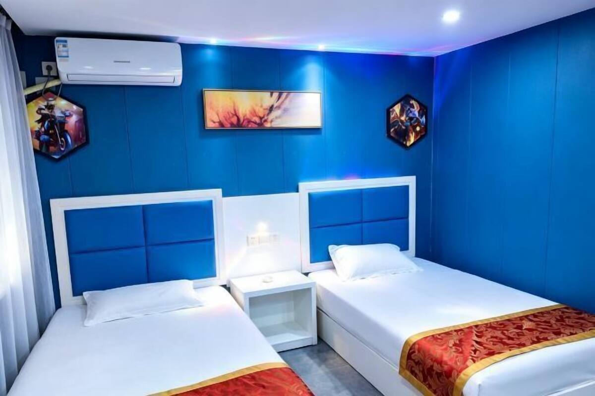 Habitación de hotel con dos camas, una mesita de noche y aire acondicionado instalado en la pared.