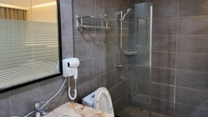 Ένα σύγχρονο μπάνιο με ένα διαχωριστικό από γυαλί για την καμπίνα ντους, έναν πάγκο από μάρμαρο, μια τουαλέτα και έναν καθρέφτη με περσίδες.