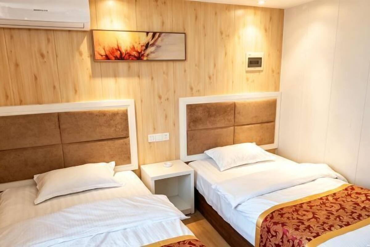 Habitación de hotel con dos camas, paredes de paneles de madera, aire acondicionado y una mesita de noche con lámpara.