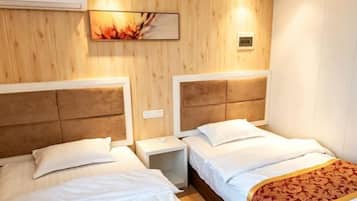 Hotelkamer met twee bedden, houten paneelwanden, een wandairconditioner en een klein nachtkastje met een lamp.