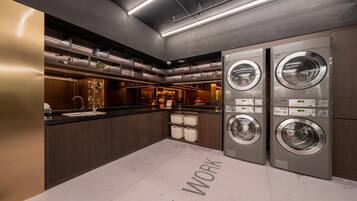 A modern laundry room with stainless steel appliances, a counter, and baskets.