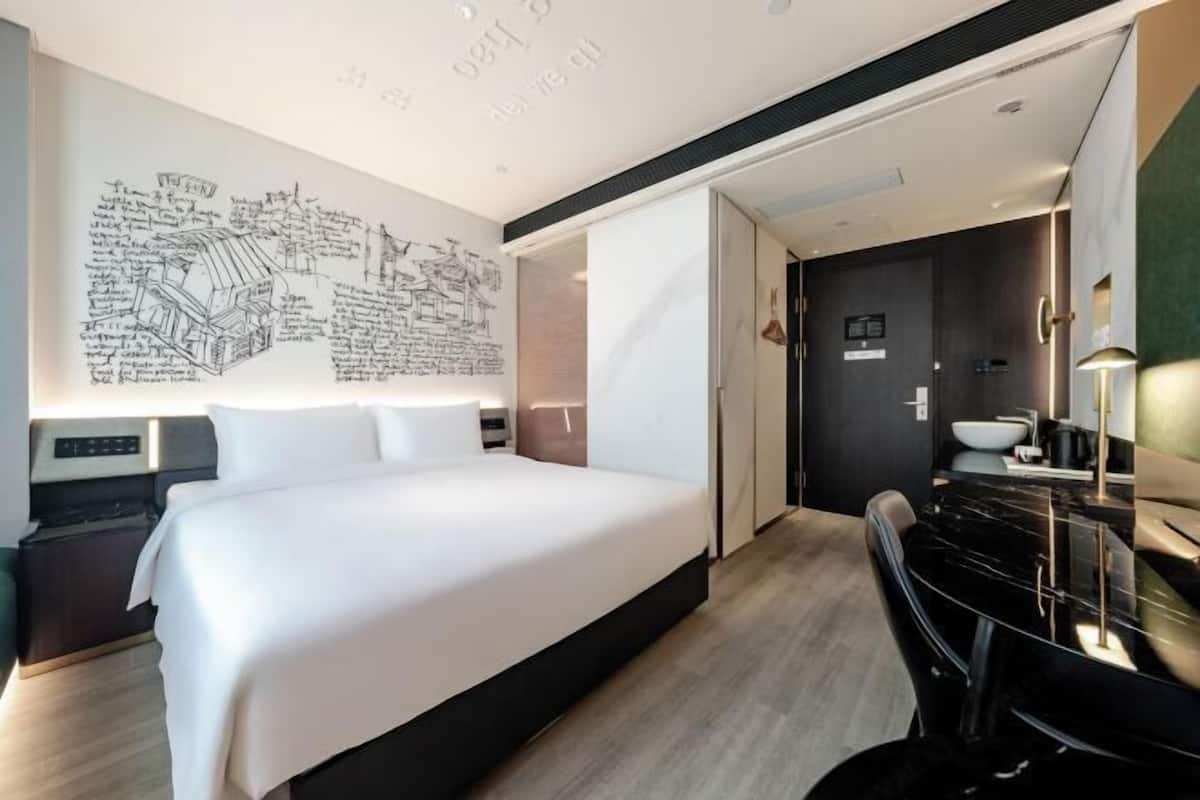 A modern hotel room with a large bed, a desk, a mirror, and a wall with a map.