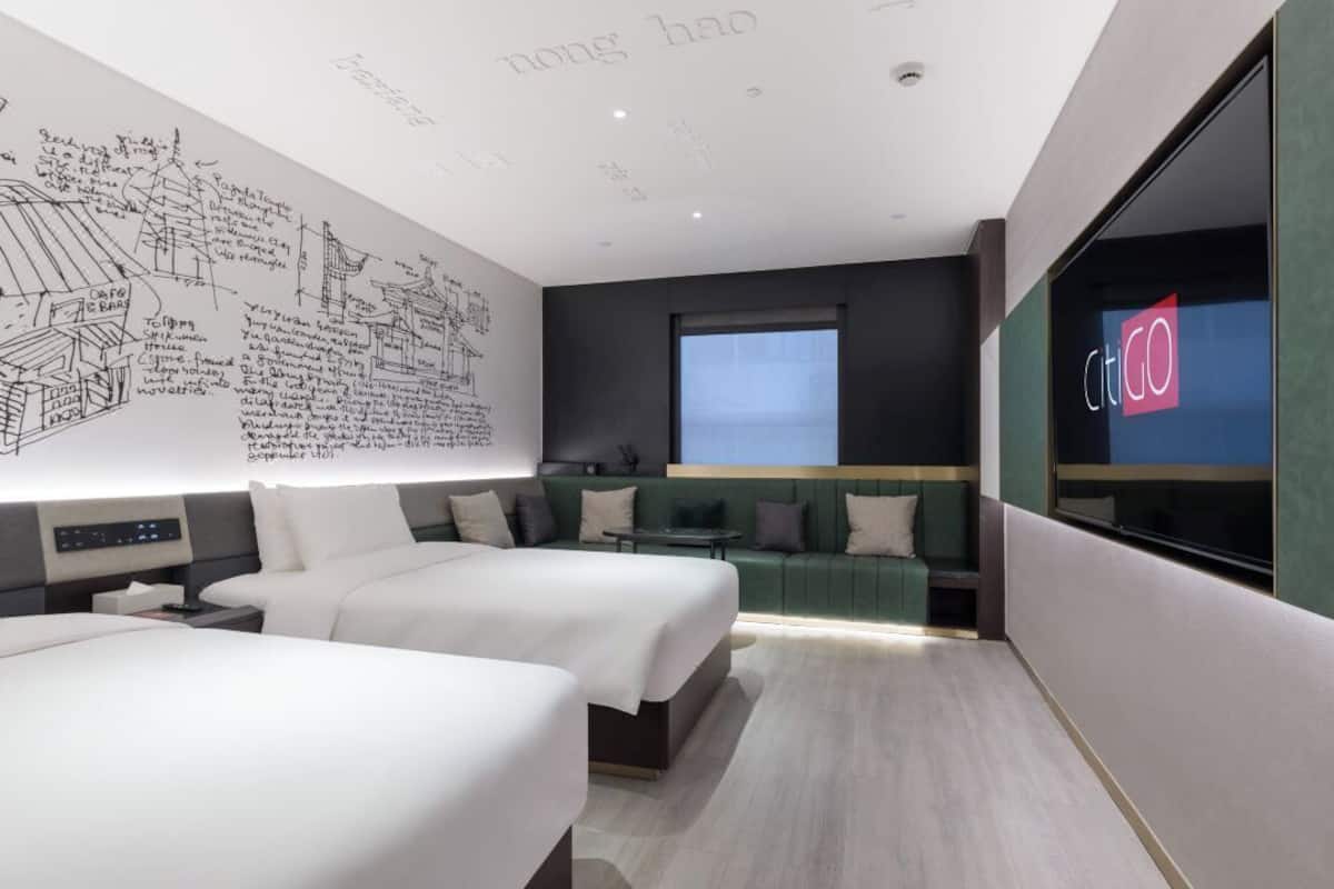 A modern hotel room with two beds, a large wall mural, a green sofa, a small table, and a window.