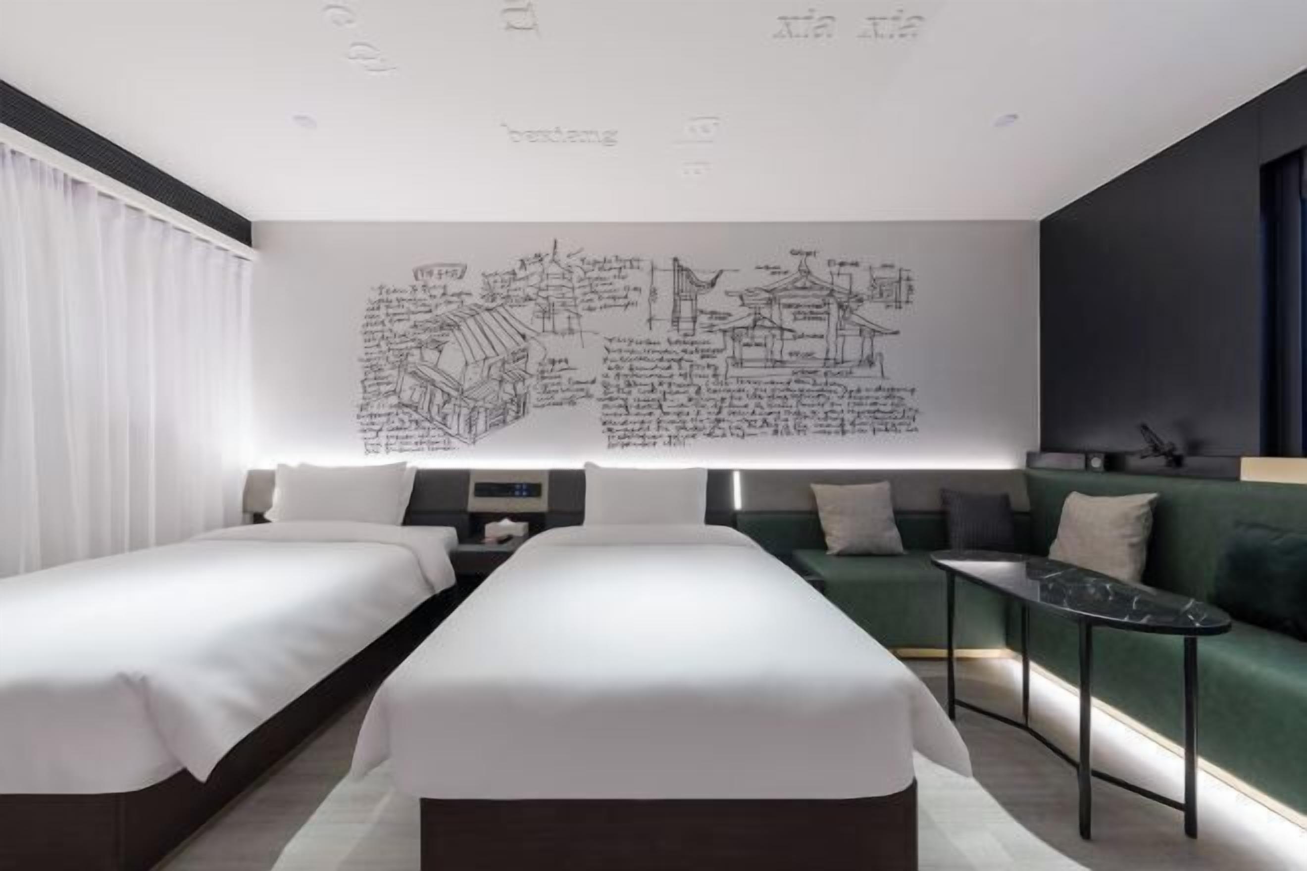 Habitació d'hotel moderna amb dos llits, un sofà verd i una taula petita.