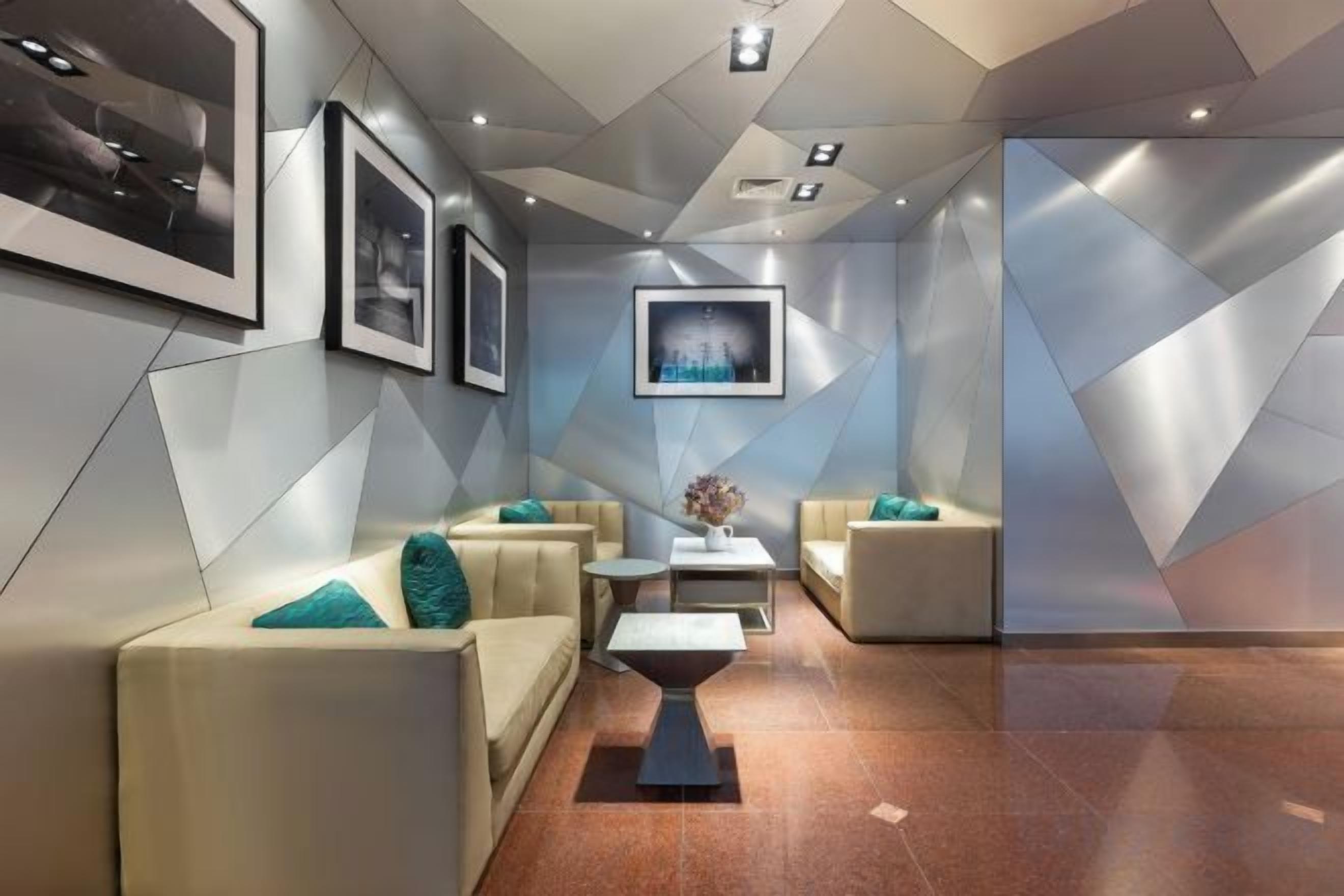 A modern lobby with a geometric wall design, seating area with couches and a coffee table, and framed artwork on the walls.