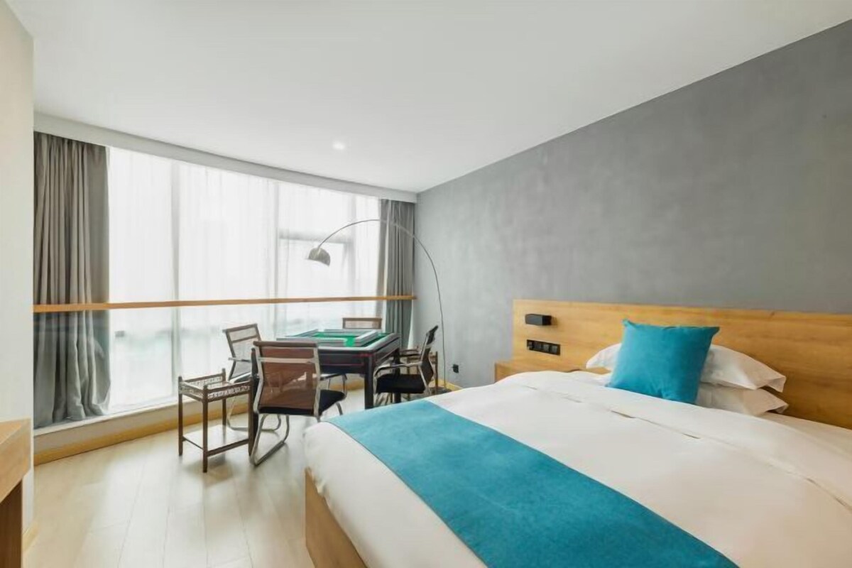 Ein Hotelzimmer mit einem Bett, einem Schreibtisch mit Stühlen, einem großen Fenster und Blick auf die Stadt.