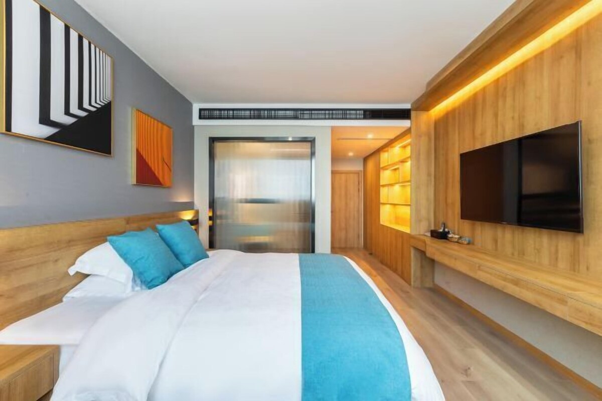 Ein modernes Hotelzimmer mit einem großen Bett, einem an der Wand montierten Fernseher und einer Holzpaneelenwand.