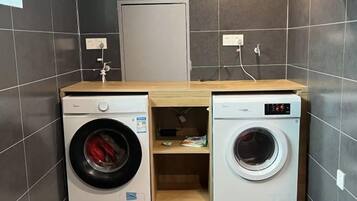 Een kleine wasruimte met twee wasmachines, een houten aanrechtblad en een deur op de achtergrond.