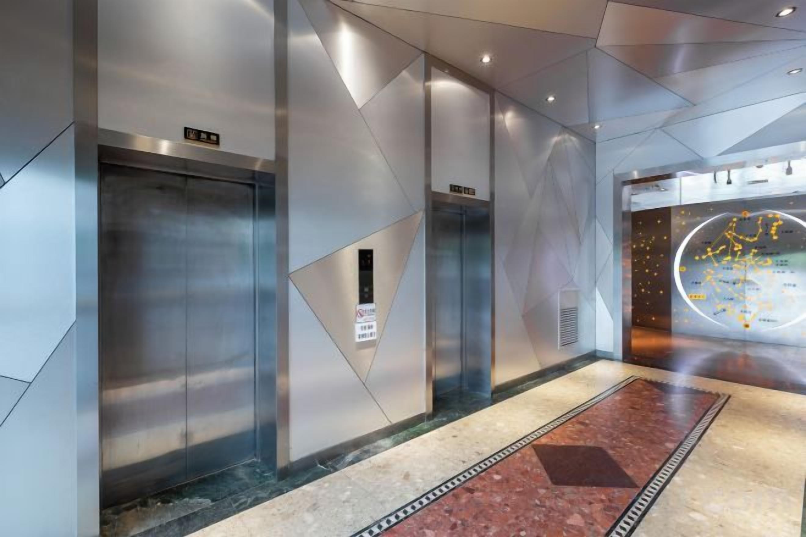 Un intérieur comprenant deux ascenseurs, un sol à motifs et un mur doté d’un écran numérique.