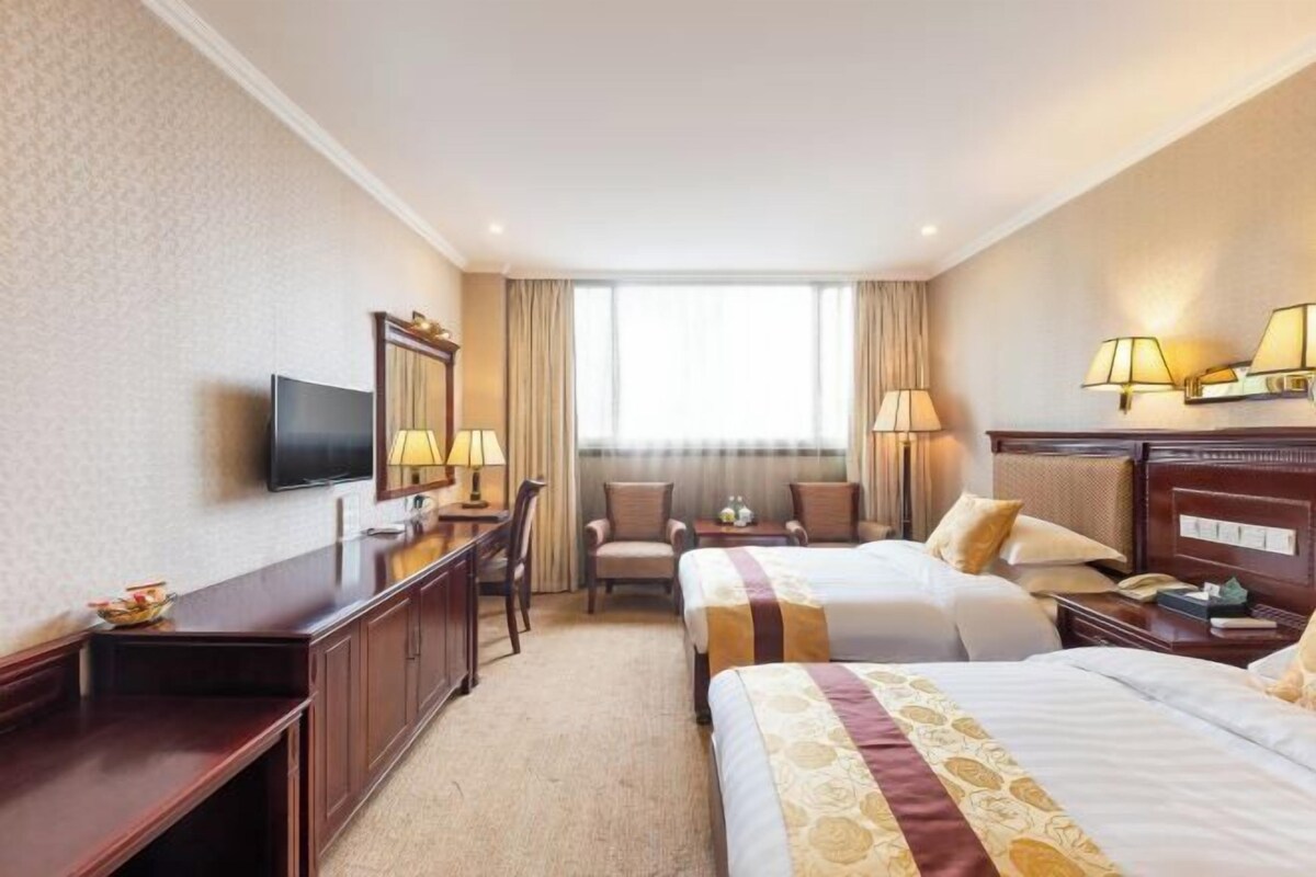 Ein Hotelzimmer mit zwei Betten, einem Schreibtisch, einem Stuhl, einem Fernseher und einem Fenster mit Vorhängen.