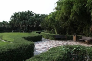 Um jardim ajardinado com um caminho pavimentado, bancos e sebes bem aparadas.