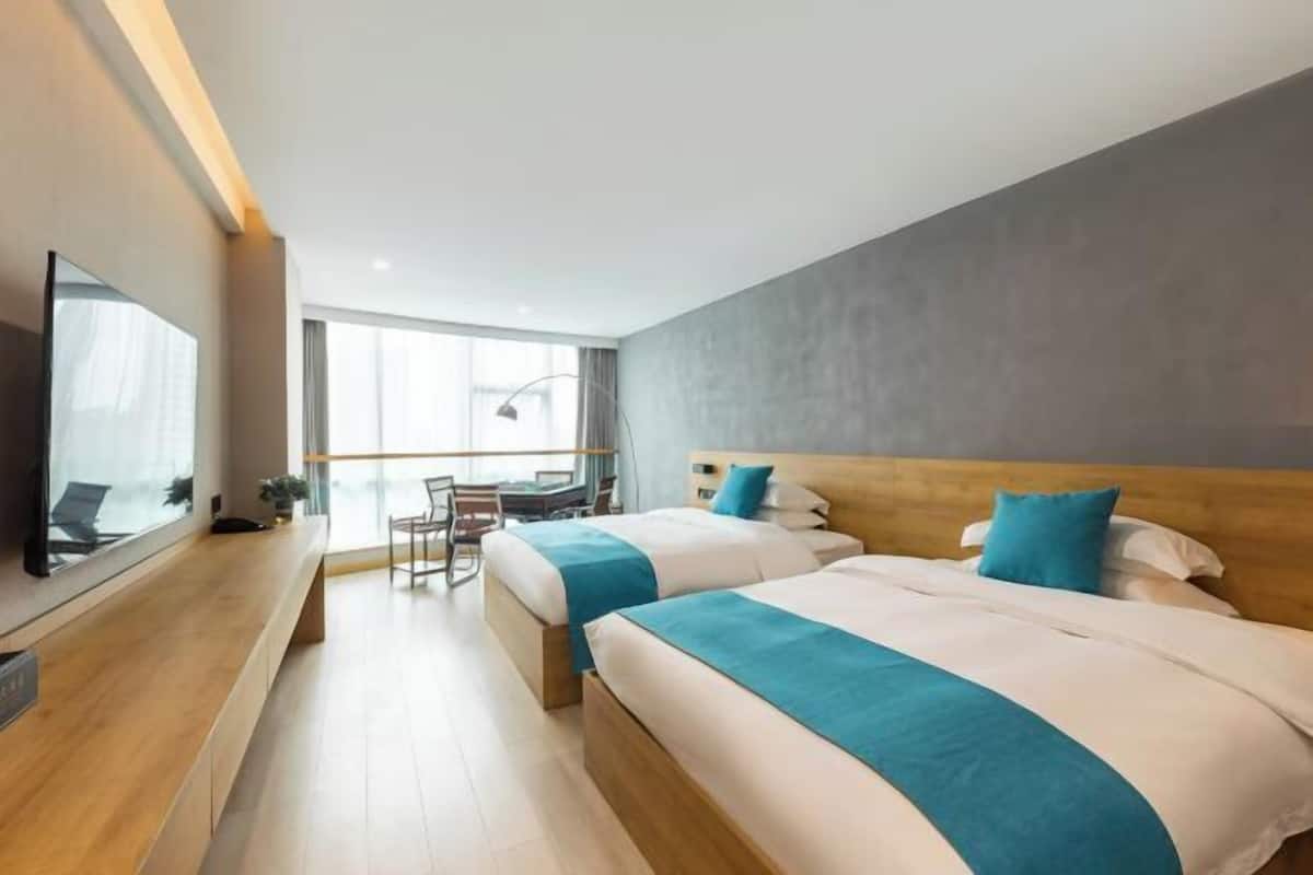 A hotel room with two beds, a desk, a chair, a large window, and a TV.
