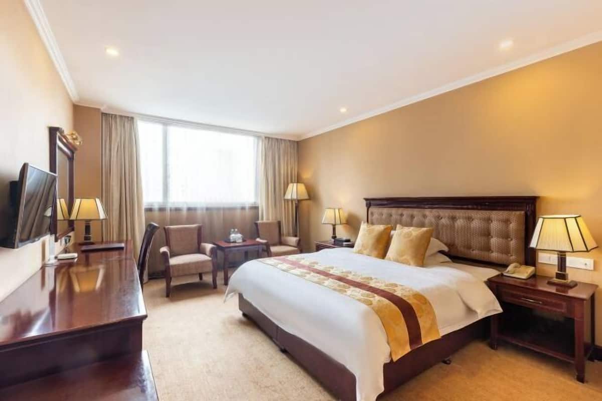 A hotel room with a large bed, two bedside tables, a desk, a chair, a TV, and a window with curtains.