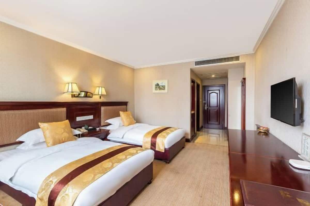 A hotel room with two beds, a desk, a flat-screen TV, and a framed picture on the wall.