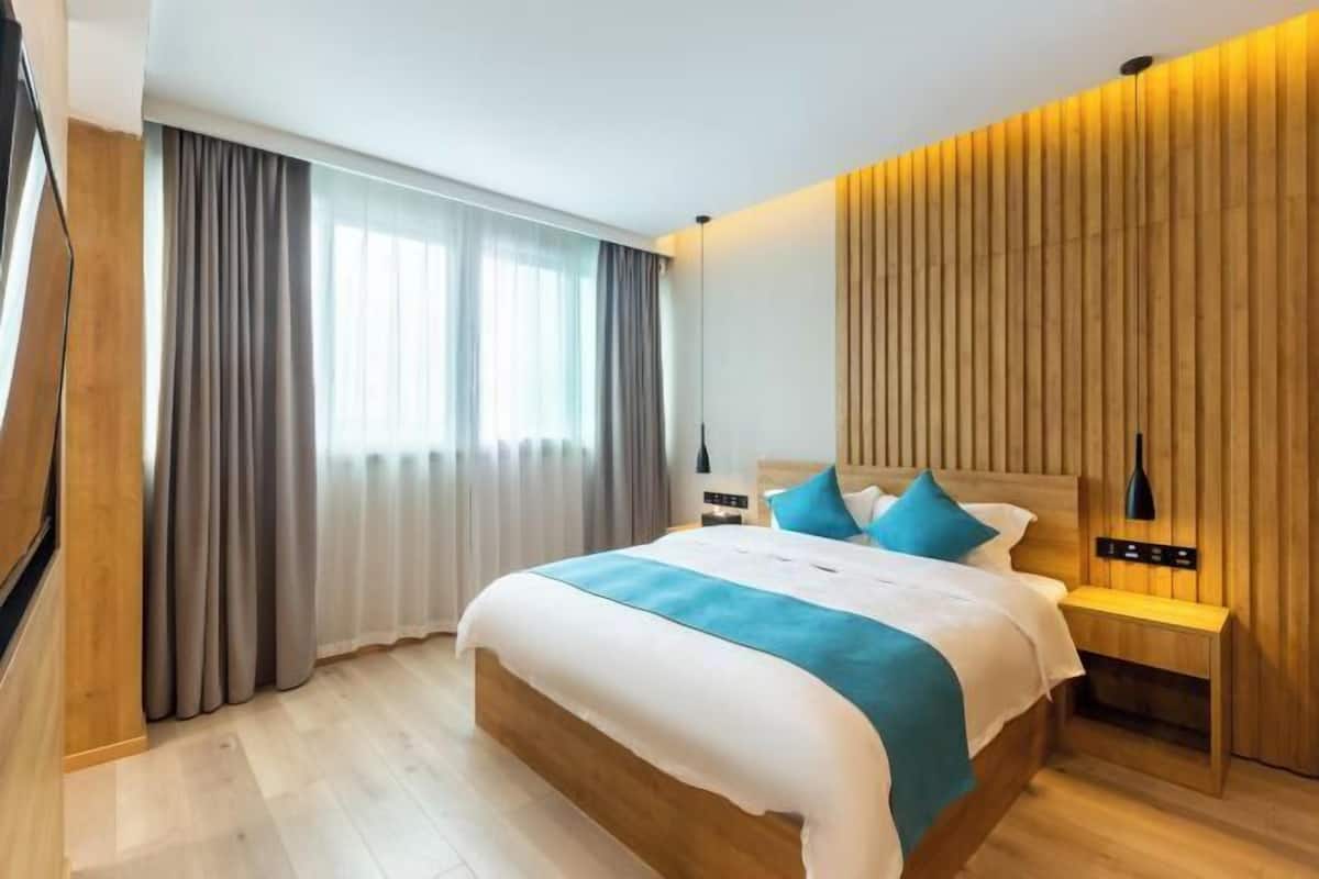 A modern hotel room with a wooden bed, a nightstand, a lamp, and a large window with curtains.