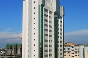 Edifício de vários andares com design arquitetônico moderno, destacando uma fachada de vidro central e uma série de varandas.