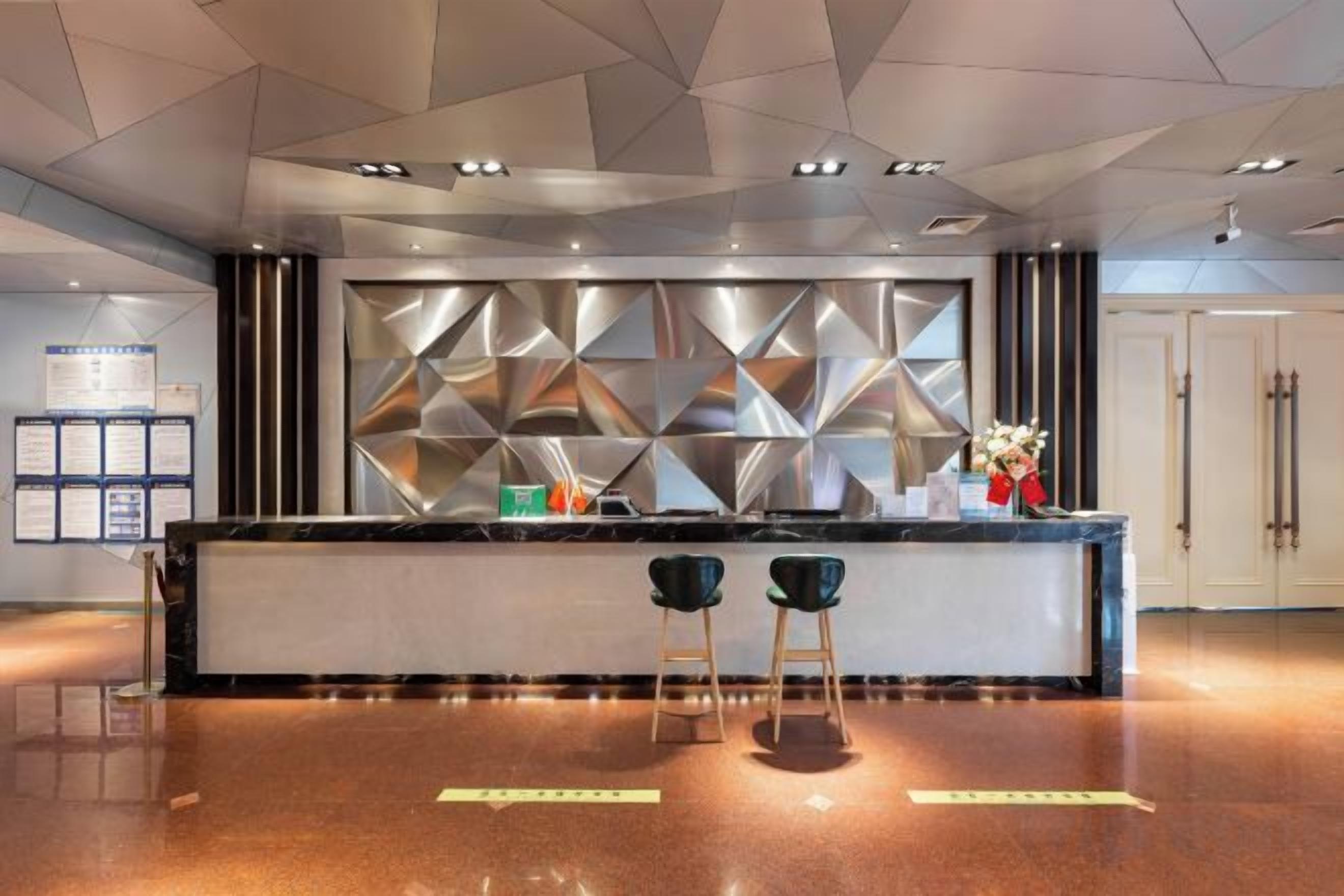 A modern reception area with a geometric wall design, a reception desk, two bar stools, and a polished floor.